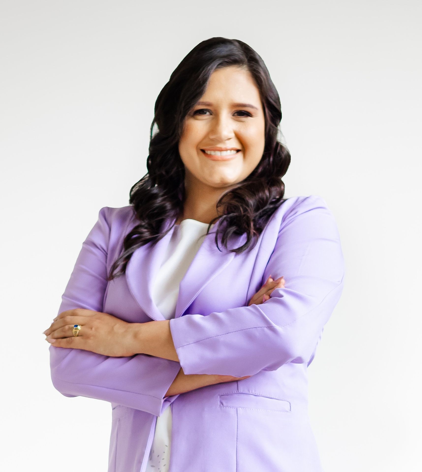 Person in a light purple blazer, smiling with crossed arms against a plain white background.