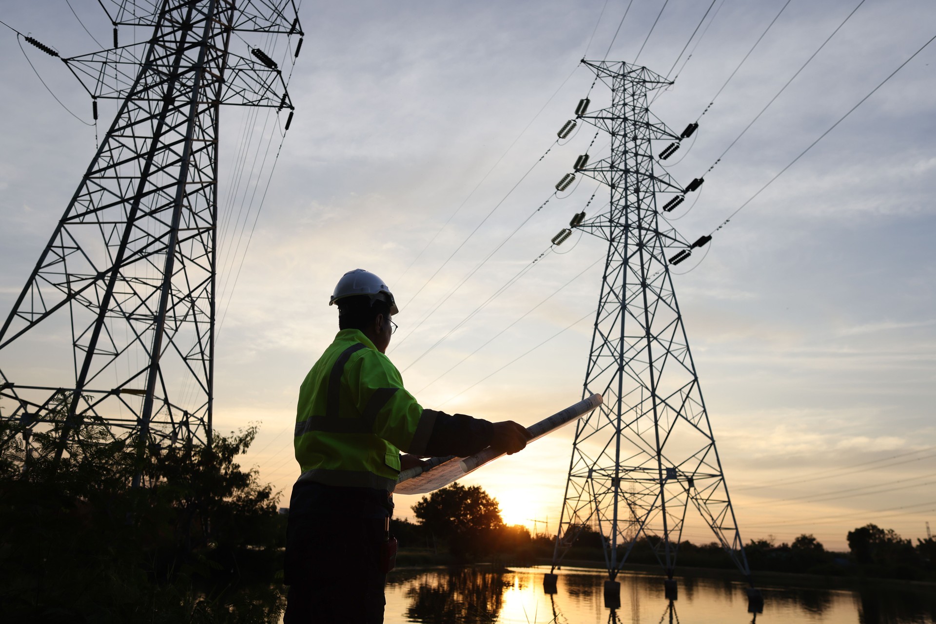 Senior electrical engineer with PPE uniform works on drawing at the power plant  of High voltage Electrical pole during sunset
